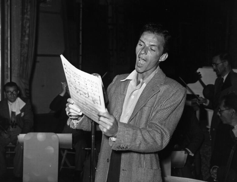 A man holds sheet music, mid singing.