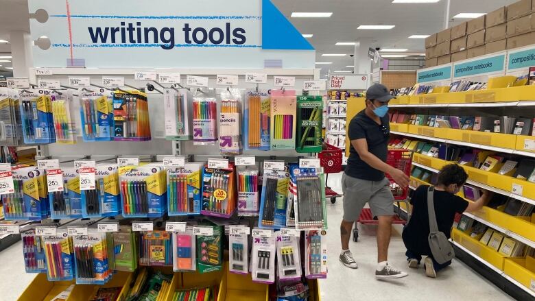 Two people wearing masks examine school supplies in the aisle of a store. 