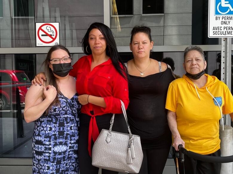 Four Indigenous women stand in front of a courthouse window. 