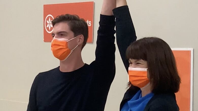 Nathaniel Teed stands beside NDP leader Carla Beck. She's holding his arm and raising it in the air in victory.