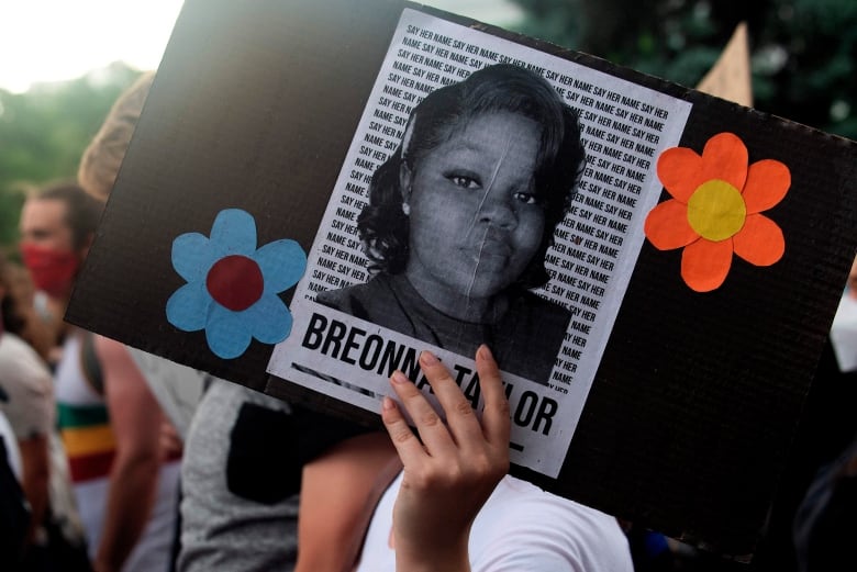 A photograph of a young Black woman pasted on a sign is held by a demonstrator.