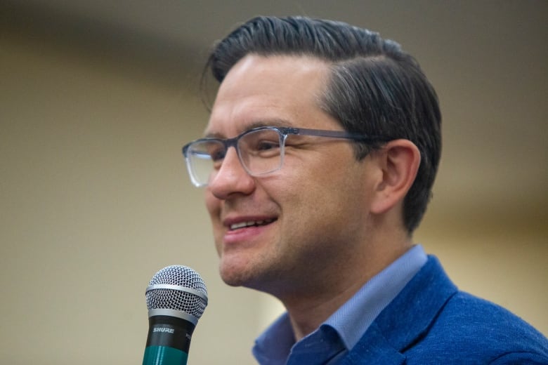 Man in glasses smiling, holding microphone.