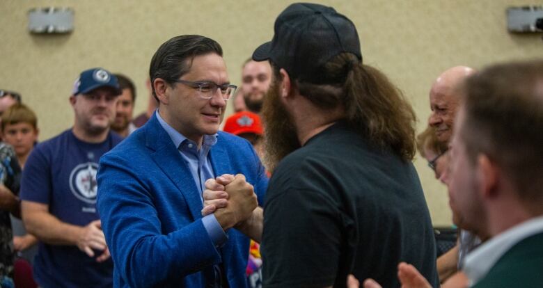 Man in blue suit grabs hand of bearded person in ballcap.