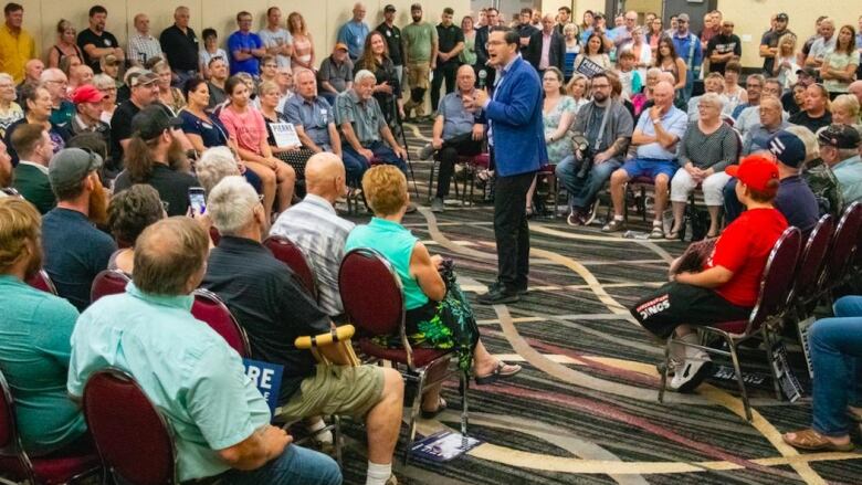 Man in blue suit surrounded by people in chairs circled around him.