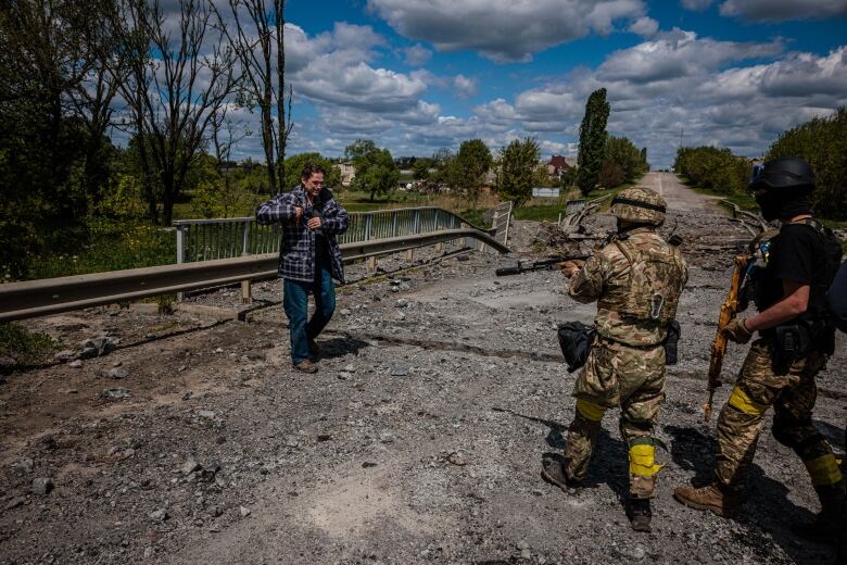 Two men holding guns speak with another man on a road. 