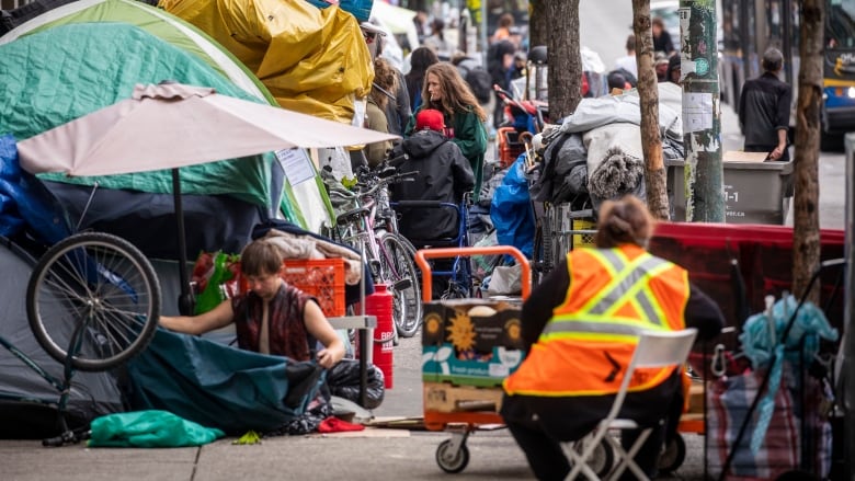 A group of people meet and talk near a row of tents on a sidewalk.