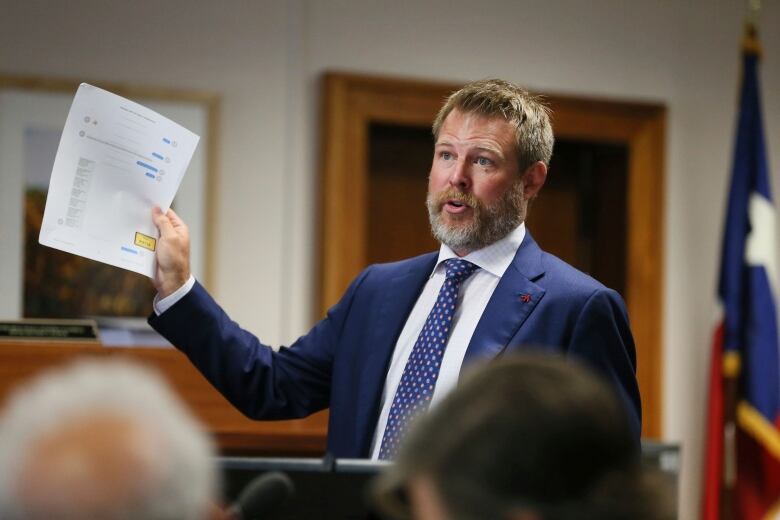 A man in a courtroom holds up papers for the jury to see. 