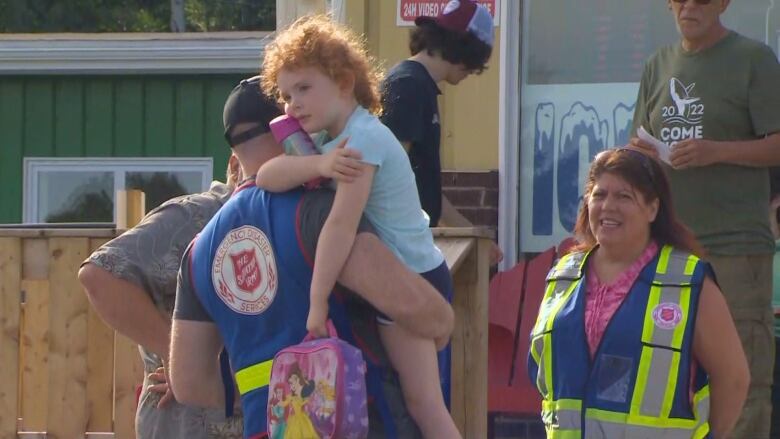 One man in a blue vest with the Salvation Army crest on the back holds an exhausted young child with curly hair.