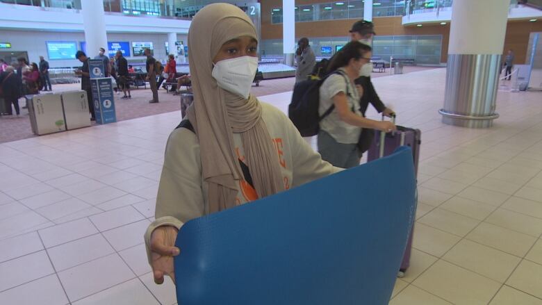 A woman holds a yoga mat in an airport.