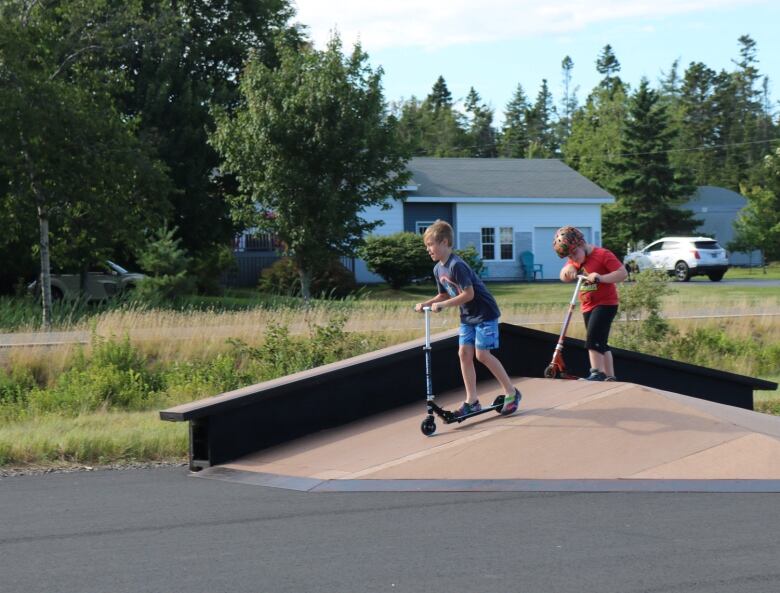 Two boys use their scooters to ride down a ramp. 