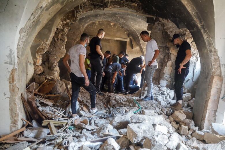 Several people walk inside a structure filled with rubble.