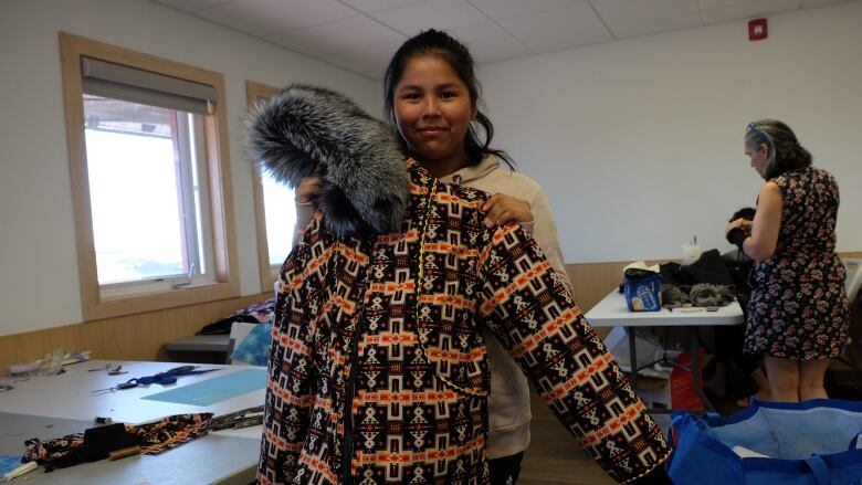 A 15 year old girl from Behchoko, N.W.T. holds up her orange and yellow printed parka that her little sister will wear to school this winter.