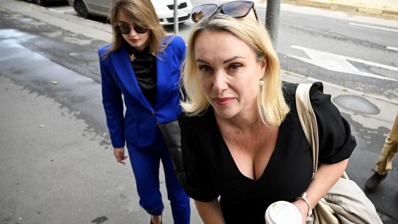 A blonde-haired woman in a black top enters a court building.