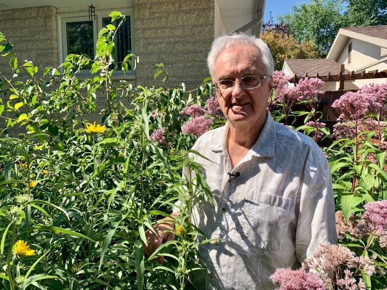 A man stands in some tall grass and flowers.