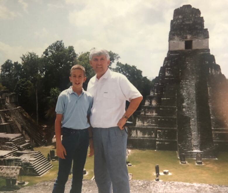 A man wih grey hair and an adolescent boy stand in front of some Guatamalan pyramids.