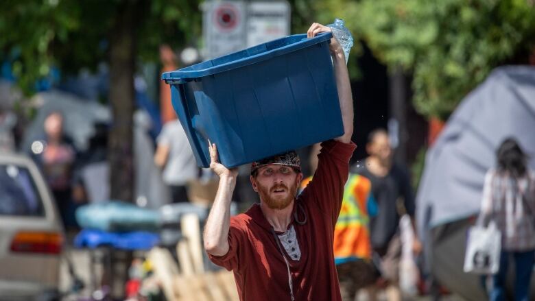 A person holds a blue bin above their heads on a street.