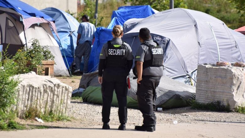 Two security officers look onto a field of tents.