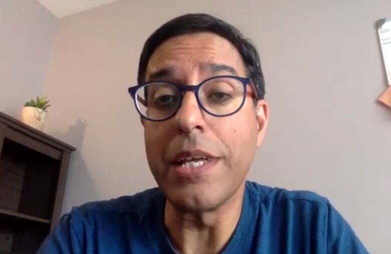 A man wearing a blue shirt and black glasses mid-speaking