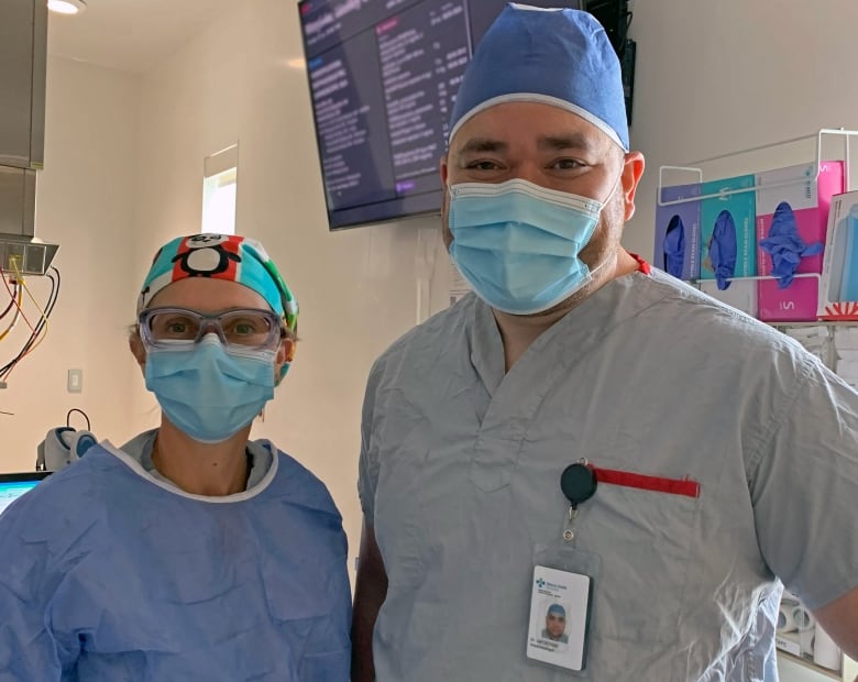 Two anesthesiologists  a woman and a man  stand inside a hospital, wearing a mask and scrubs.