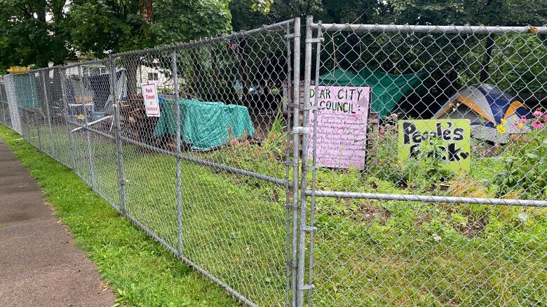 Signs and empty tents at Meagher Park are seen through a metal fence