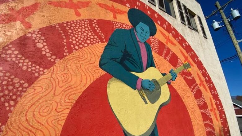 A mural of a Black man with a guitar. He is pictured against a red background with a bird design.