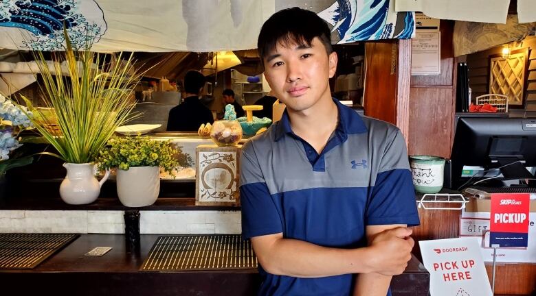 Eric poses for the camera in front of a sushi bar counter. He is an Asian man wearing a blue and grey Under Armour t-shirt.