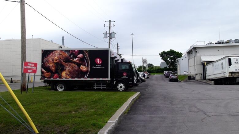 A black truck with a red and white PG logo and a photo seasoned chicken sits in the parking lot in front of an industrial building.