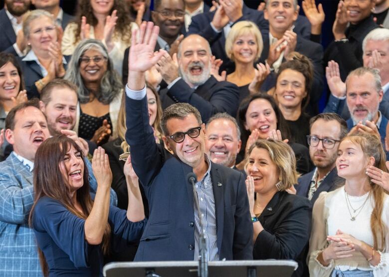 A man waves at audience with people behind him