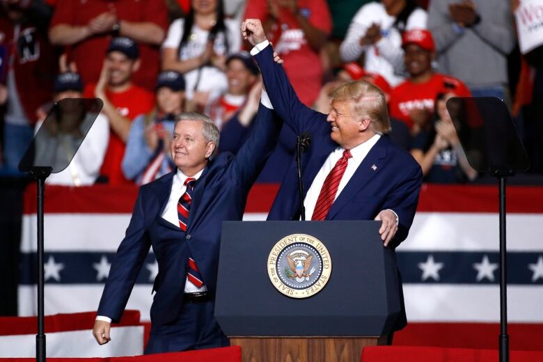 Two men clasping hands in the air in front of a crowd of people. 