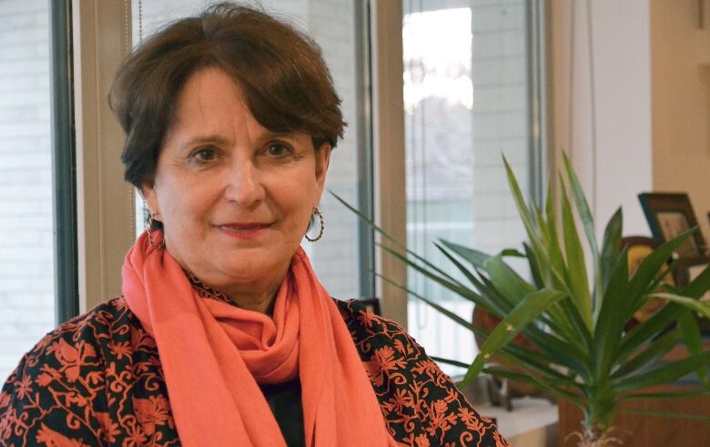 A woman with short brown hair wearing a coral paisley shirt and coral scarf