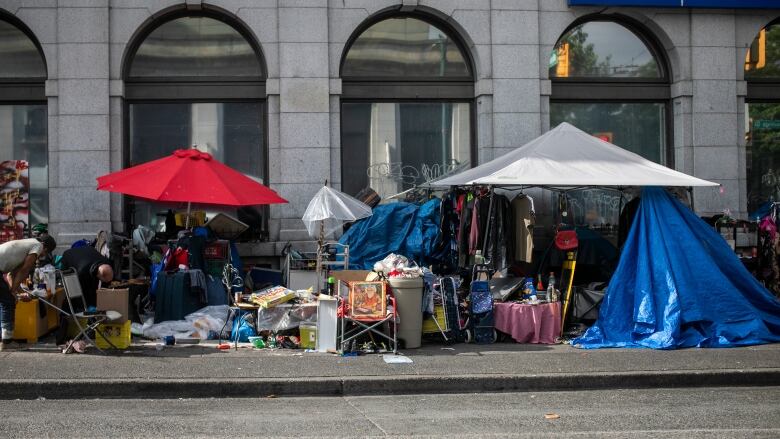 A number of tents, umbrellas, and paraphernalia lie on a pavement in front of a bank.