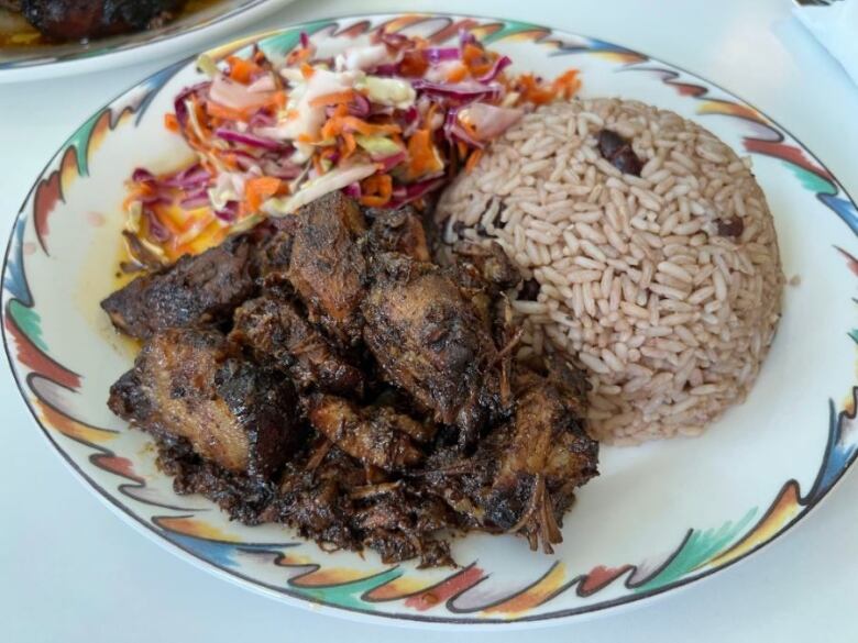 A plate is filled with jerk pork, rice and beans, and coleslaw.