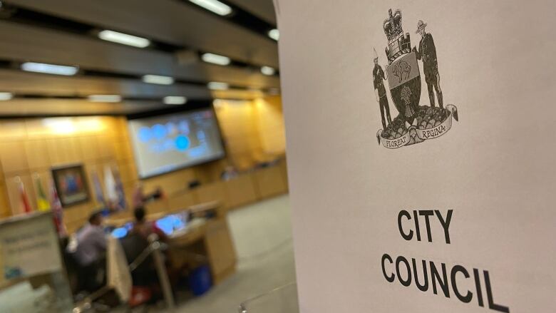 A Regina city council agenda is interposed with the city council chambers. 