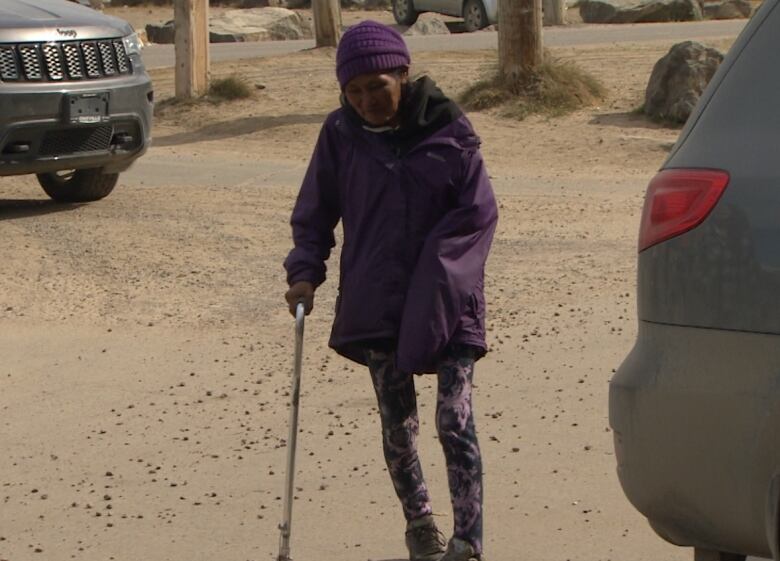 Head to toe shot of small, thin woman leaning on a cane. 