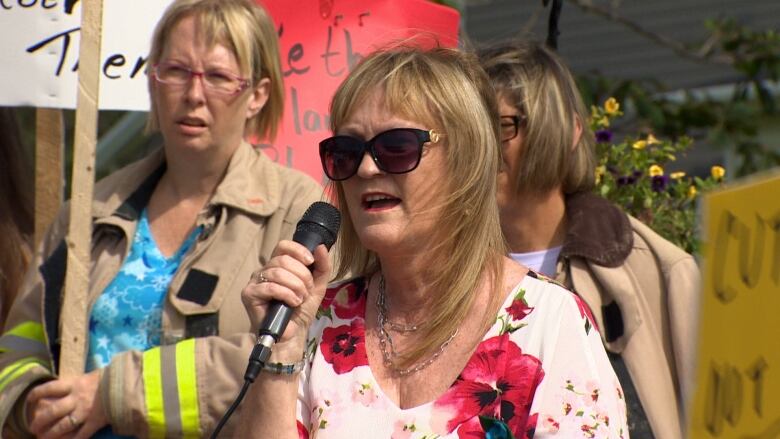 A woman speaks to a crowd holding a microphone.