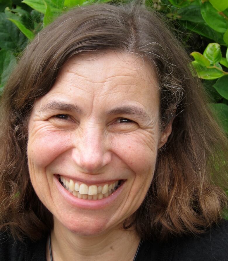 A woman smiling in front of a background of green leaves