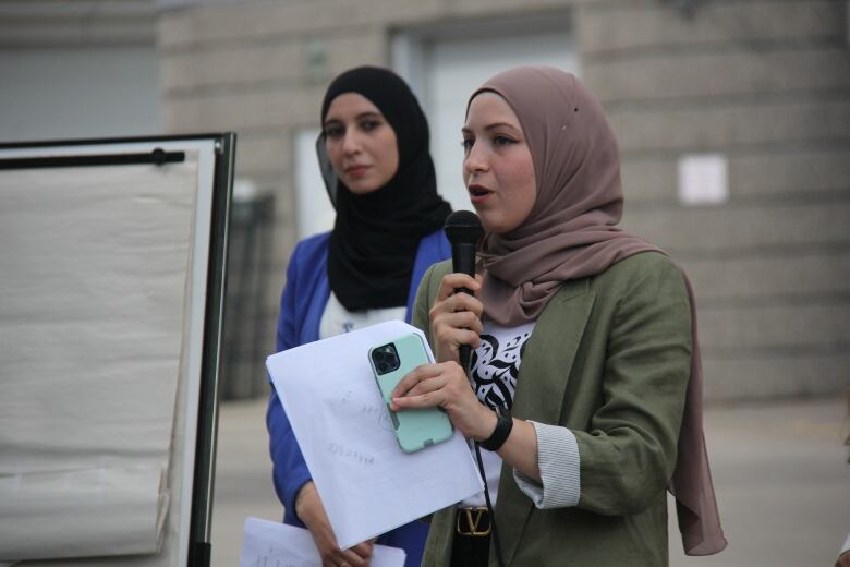 One woman speaks into a microphone while another woman looks on.