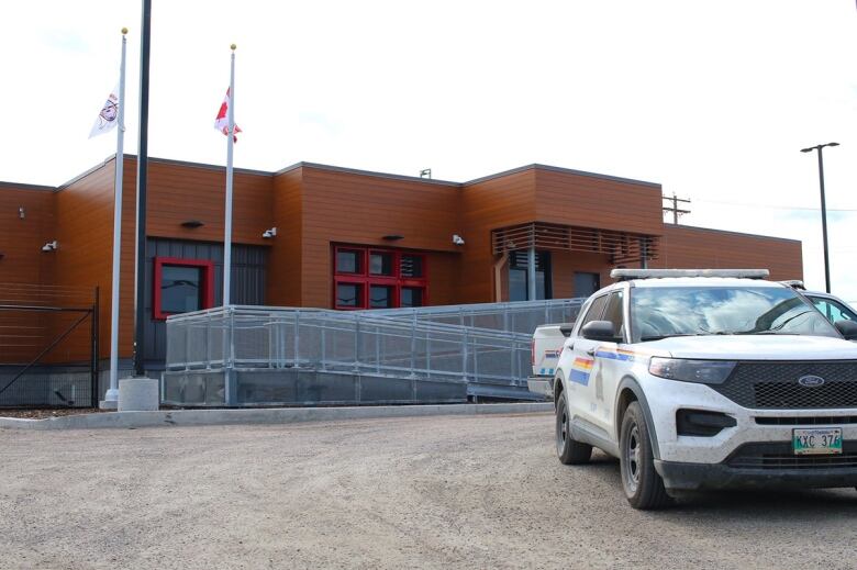 A police vehicle sits in a parking lot in front of a building with a brown wooden exterior.