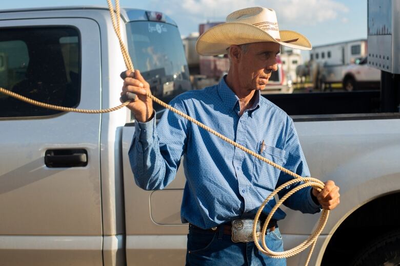 An older cowboy swings a lasso in front of a truck.