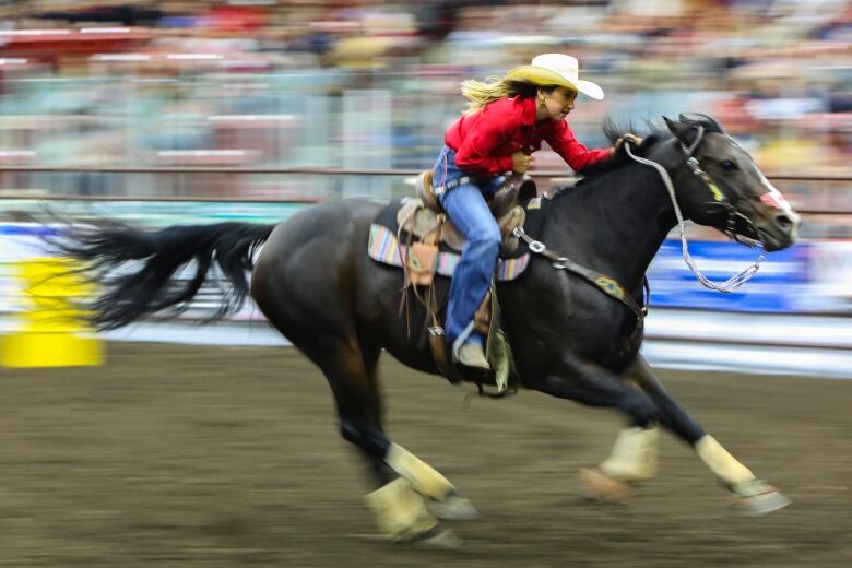 A women with a red shirt and her horse race in a barrel racing competition.