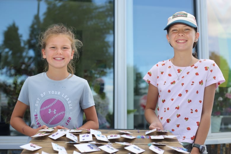 Two young girls hold a board with hand-made earings on it.