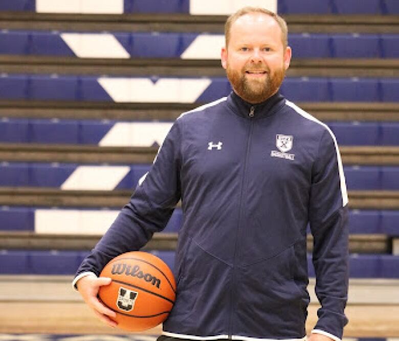 A man stands on a basketball court holding a basketball.