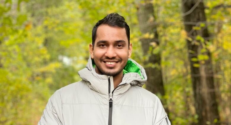 A man smiling with trees in the background. 