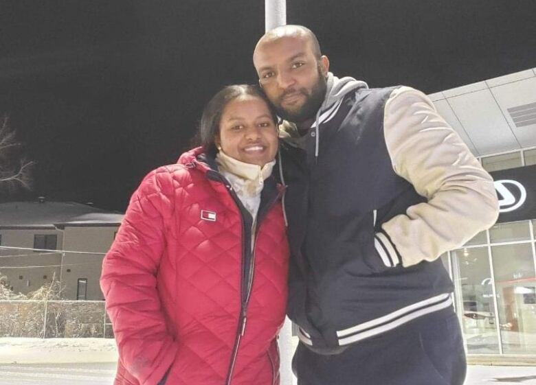 A woman in a red coat poses closely with a man in a blue and white jacket.