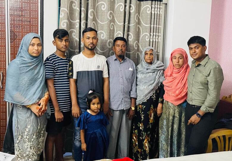 Seven adults standing in a line, with a young girl standing in the front. 