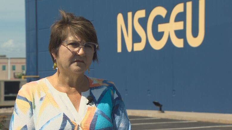 A woman with glasses stands outside in front of a big building.