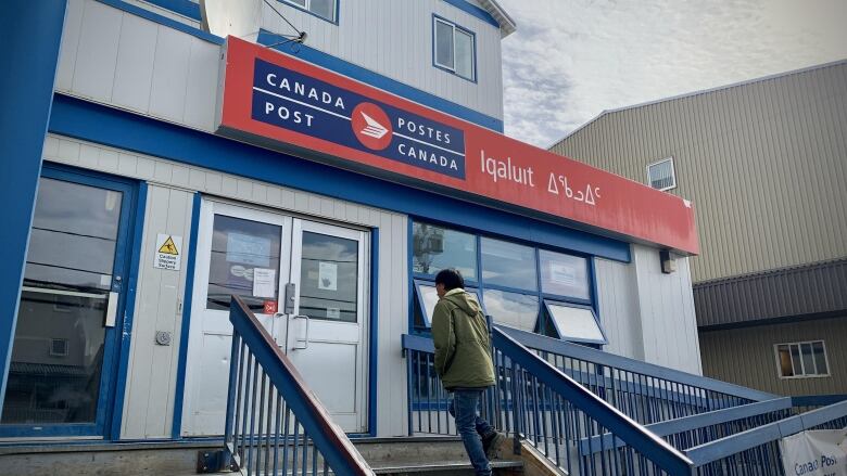 A person walks up the steps of a blue-and-white building with a big red Canada Post sign over the door.