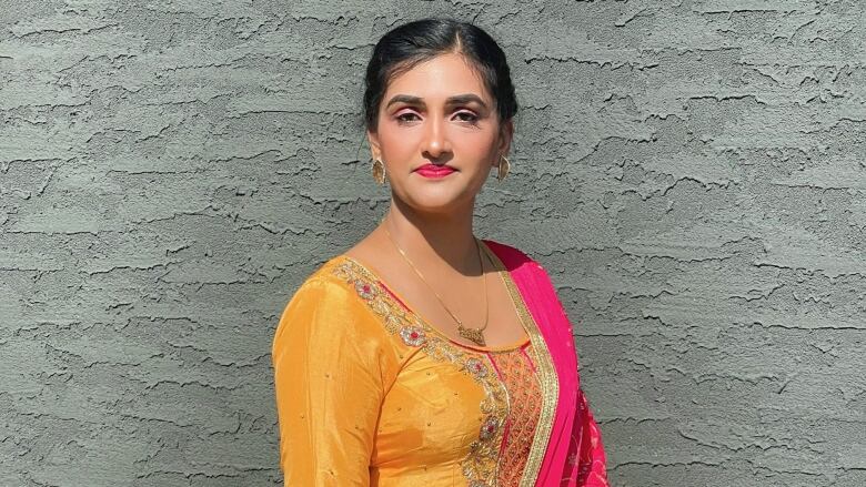 A woman wears a colourful sari in front of a grey wall.