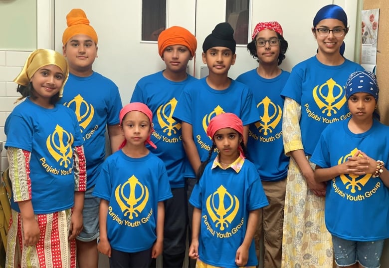 A group of children stand together wearing blue shirts that say Punjabi Youth Group