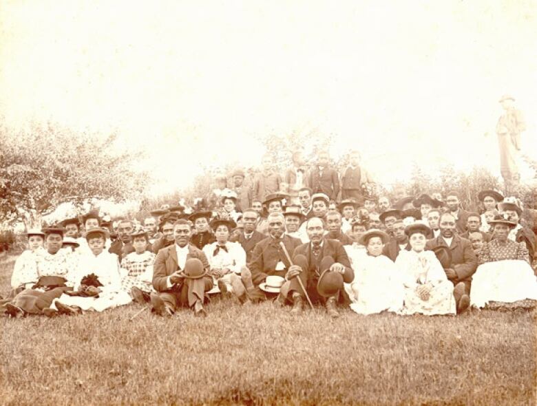 A black and white photo of a group of Black churchgoers seated on the ground.